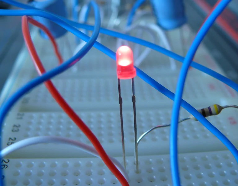 Devre tahtasına (breadboard) takılmış, yanan kırmızı bir LED, yanında direnç ve bağlantı kabloları